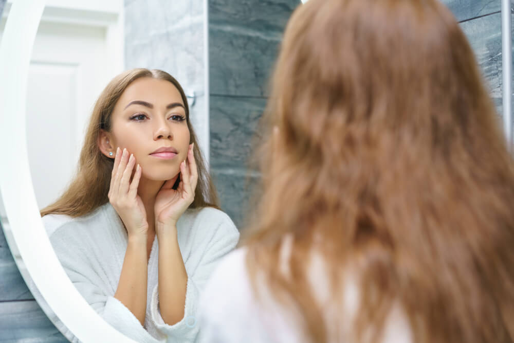 Woman looking at skin in mirror - skincare tips