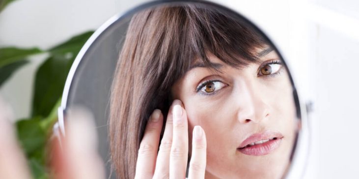 Woman looking at skin in mirror wondering how to treat wrinkle under eye