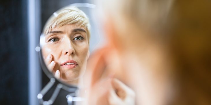 Woman looking at aging skin signs in mirror